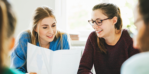 Two young women looking at class work