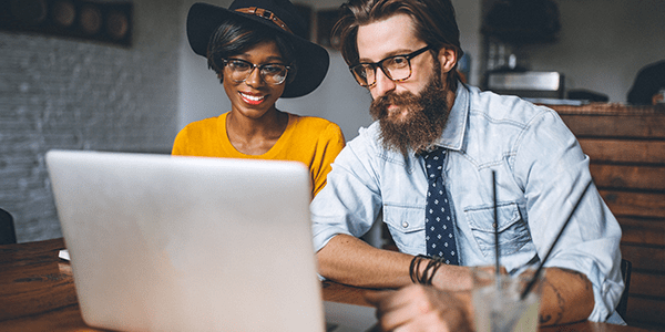 woman in hat and man with beard looking at a laptop computer