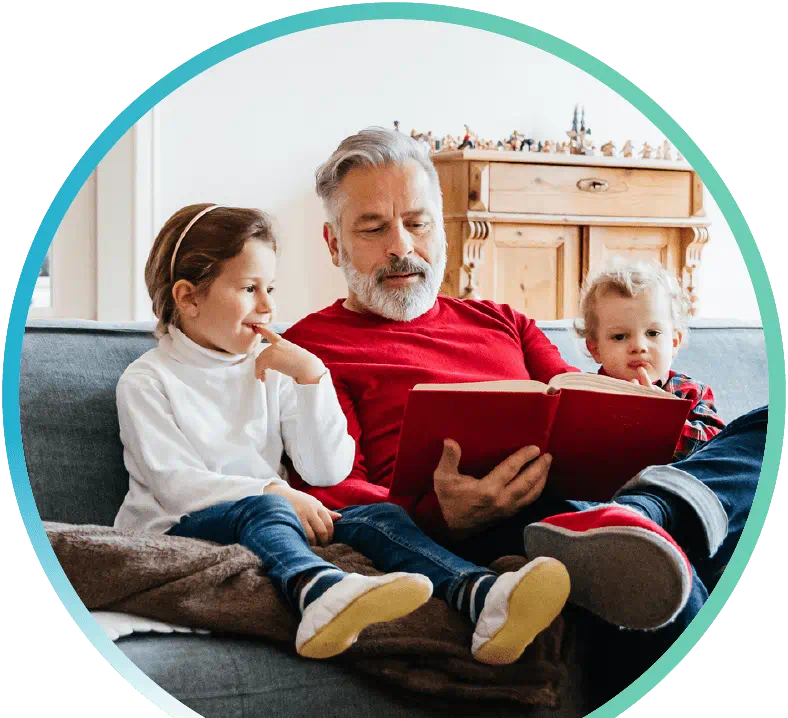 Man reading a book to two children on a sofa.