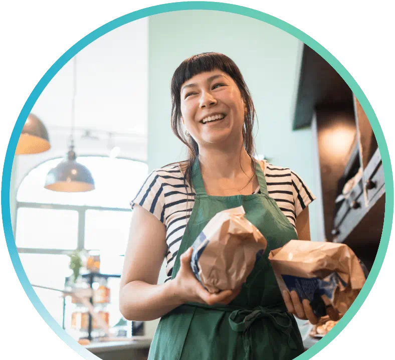 Smiling barista holding two items in brown paper bags in both hands.