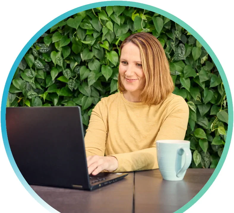 A woman typing on her laptop. Green leaves in the background.