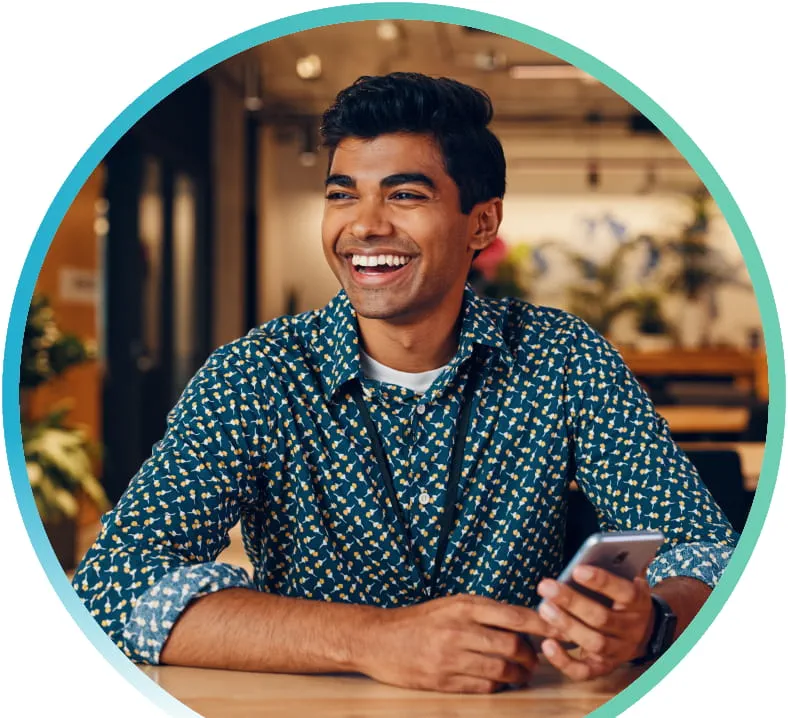 Smiling man sitting indoors at a restaurant and holding his cell phone.