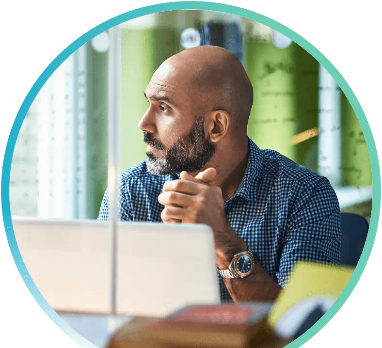 Image shows a man looking out a window with an open laptop in front of them.