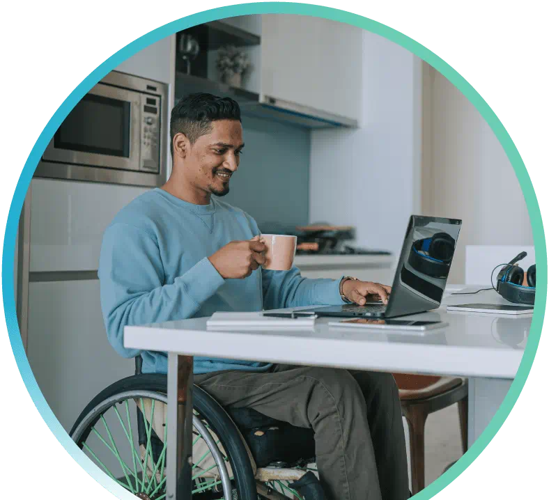 Man doing some work on a laptop, holding a mug in one hand. There is a kitchen setting in the background.