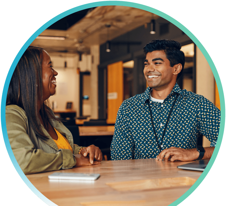 I man wearing an ID badge around his neck is sitting with a woman at a table in an office setting.