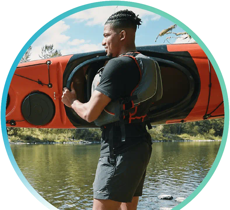 Guy carrying a kayak on a body of water.