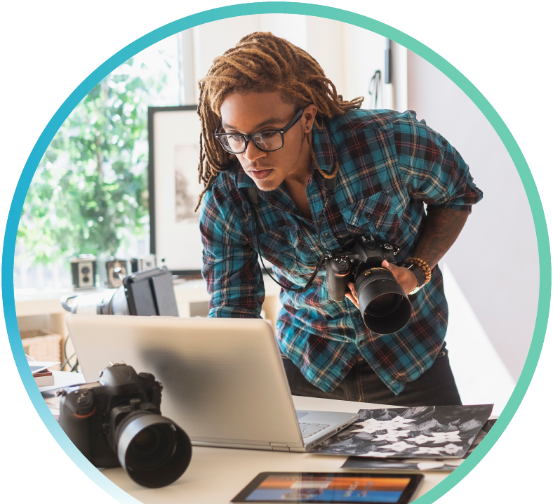 Man with a holding a digital camera in his hand while browsing on his laptop.