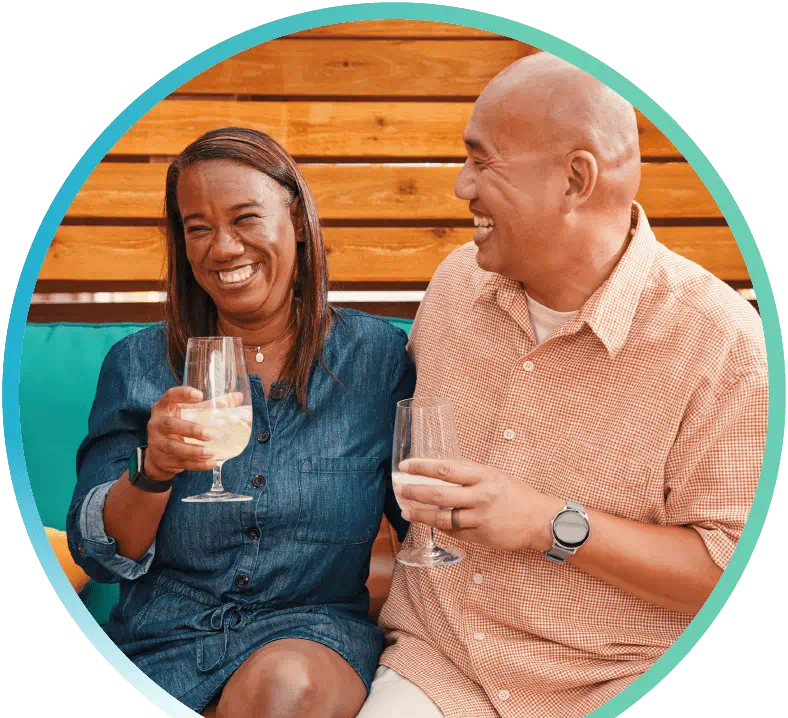 Husband and wife holding drinks and sitting on a bench.