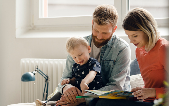 Two parents reading a book to their young child.