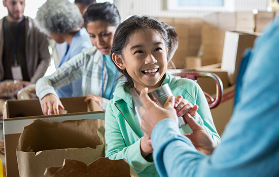 Smiling child packing canned food into brown paper bag